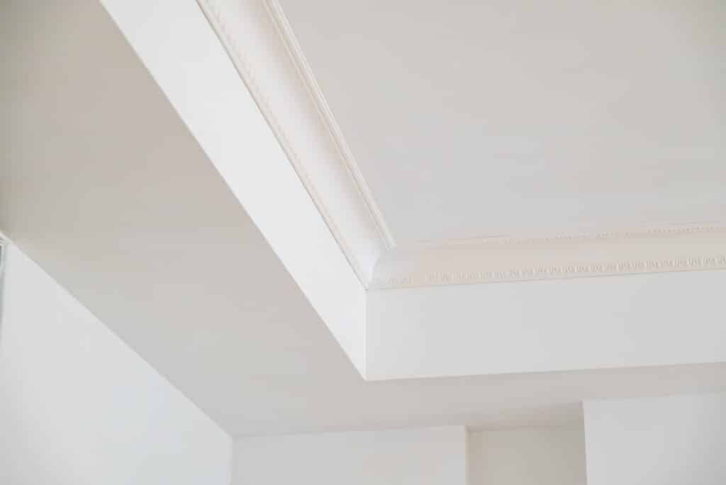 Moulures de Plafond Blanches : Élégance Intérieure Moderne Vue d'angle d'un plafond blanc avec moulures décoratives et corniche travaillée. Design intérieur moderne classique lumineux.